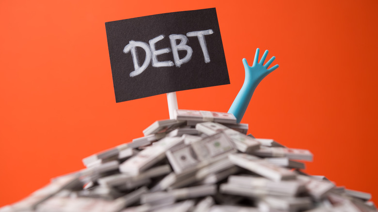 hand sticking out of a pile of money with a debt sign on top