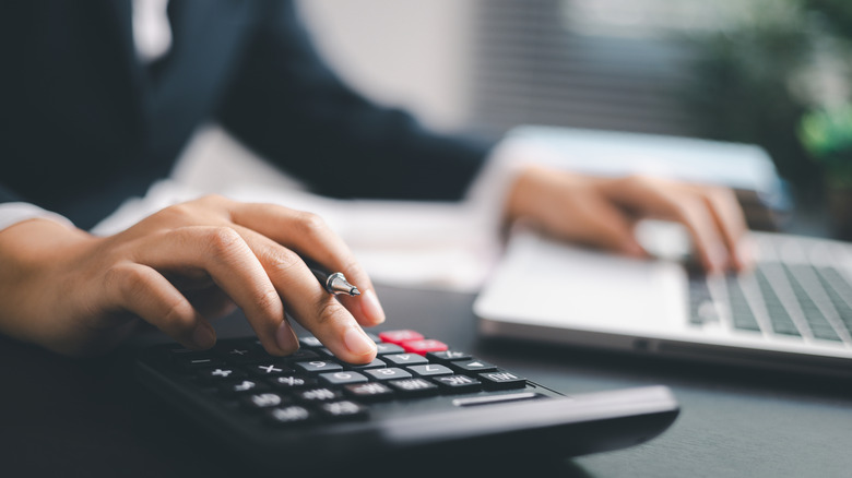 person calculating expenses on a calculator and laptop