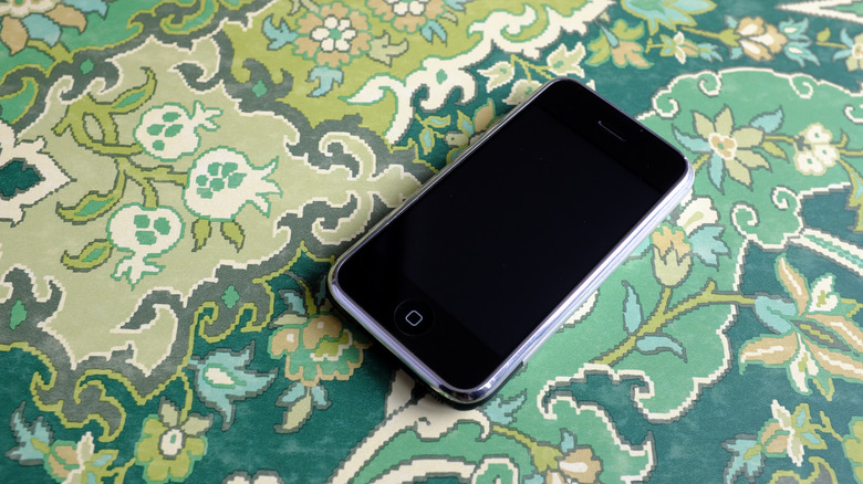 Editorial photograph of the first generation Apple iPhone 2G on green damask fabric background.