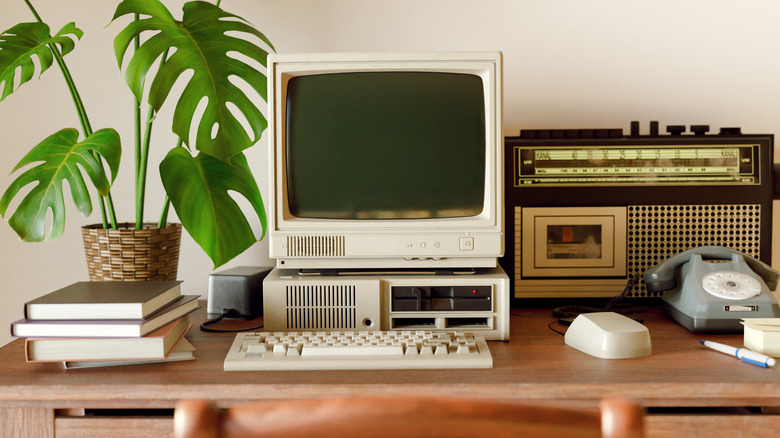 Old telephone and obsolete electronic equipment on wooden desk with plant.