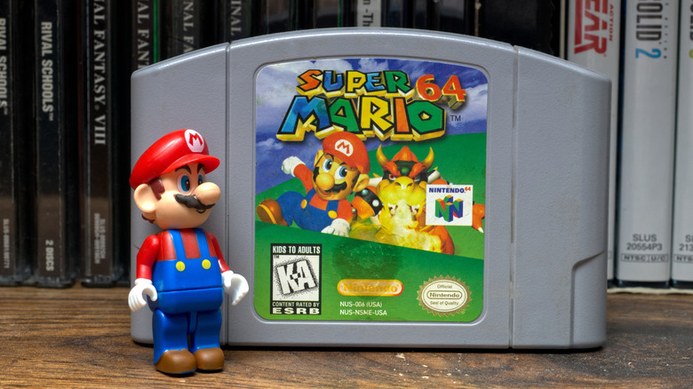 A Mario toy beside Super Mario 64 cartridge.