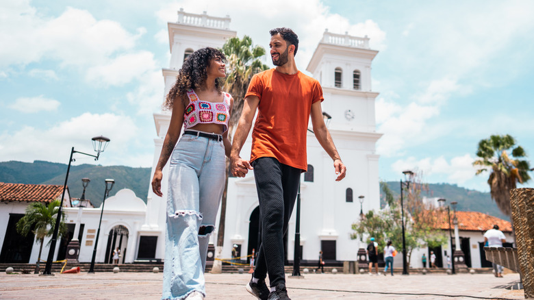 A smiling couple walking and holding hands in Bucaramanga, Colombia in a front of a large colonial building