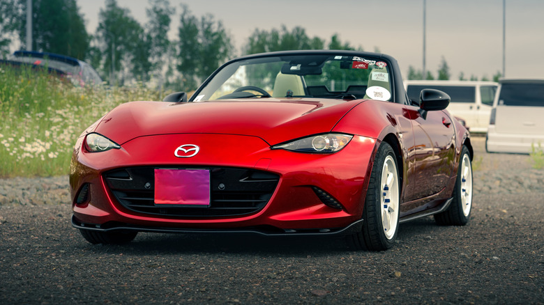 Red Mazda MX-5 Miata convertible car parked on gravel