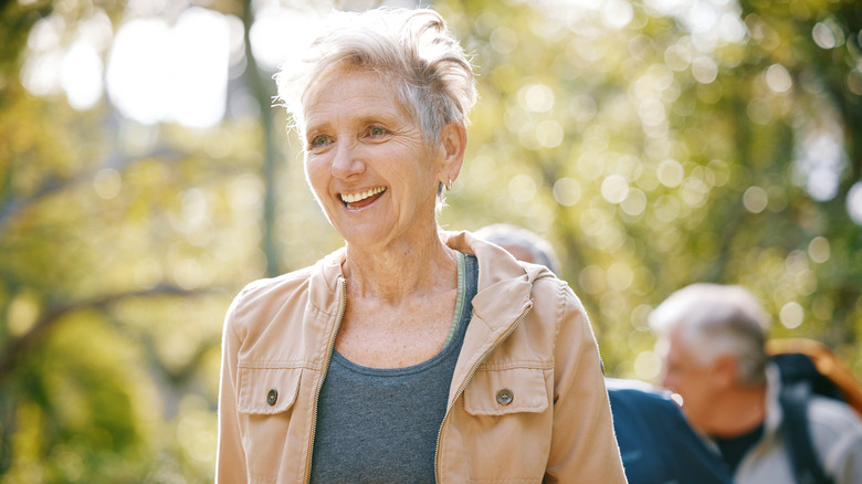 A smiling mature woman leading a group of seniors on a hike through the woods in Colorado Springs.