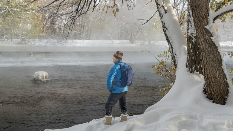 A warmly dressed mature man standing on a snow bank overlooking a river in winter in Colorado.