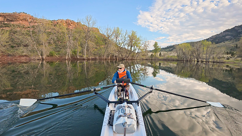 A senior man rowing a kayak on a serene lake surrounded by trees and mountains in Colorado.