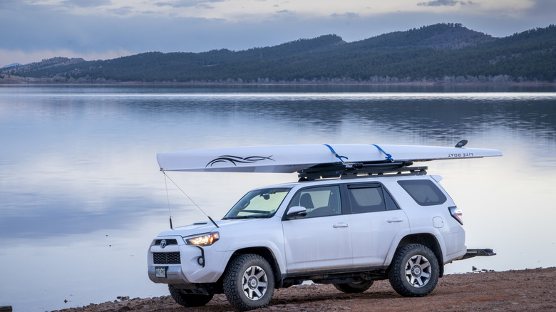 A white SUV with a canoe attached to the roof parked in front of a serene lake at dusk in Loveland, Colorado.