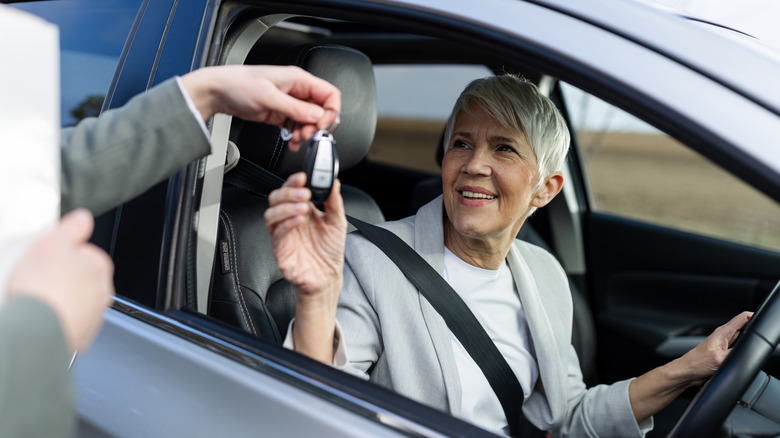 Senior woman getting keys to her new car while in the driver's seat.