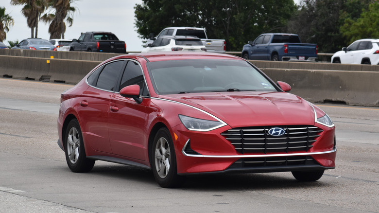 A red Hyundai Sonata sedan traveling ahead of the competition on a highway in moderate traffic
