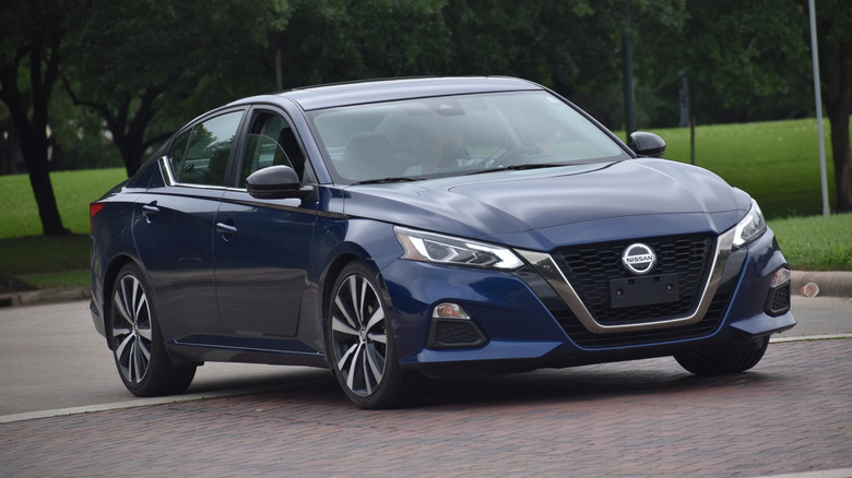 A blue Nissan Altima sedan driving on a road with a nature background.