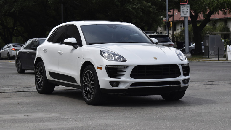 A portrait of a white colored Porsche Macan SUV cruising in a downtown district.