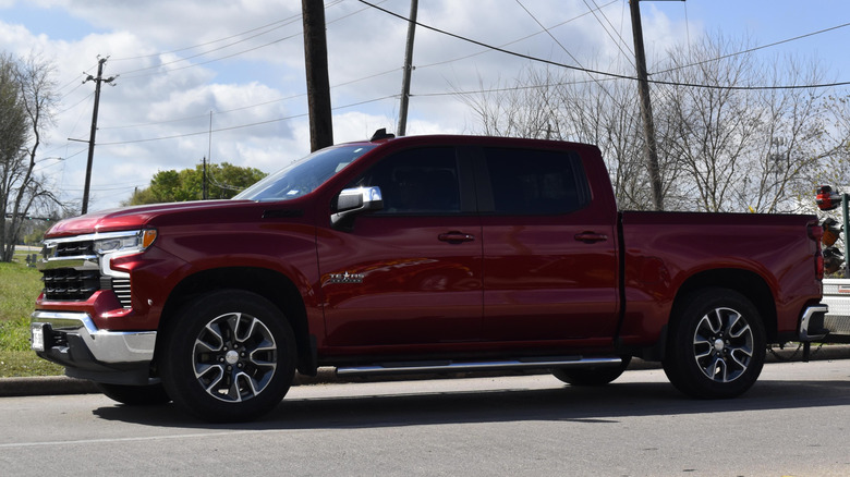 A red Chevrolet Silverado 1500 pick up truck towing construction equipment.