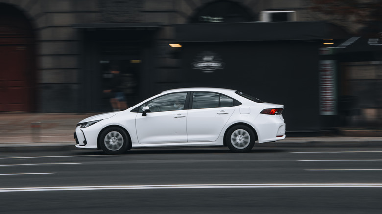 A white Toyota Corolla car moving on the street.