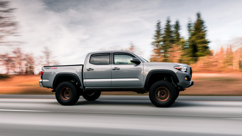 A Toyota Tacoma driving on the highway with trees in the background.