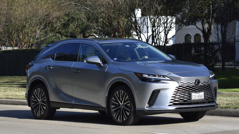 A dark grey Lexus RX driving through an upscale suburb.