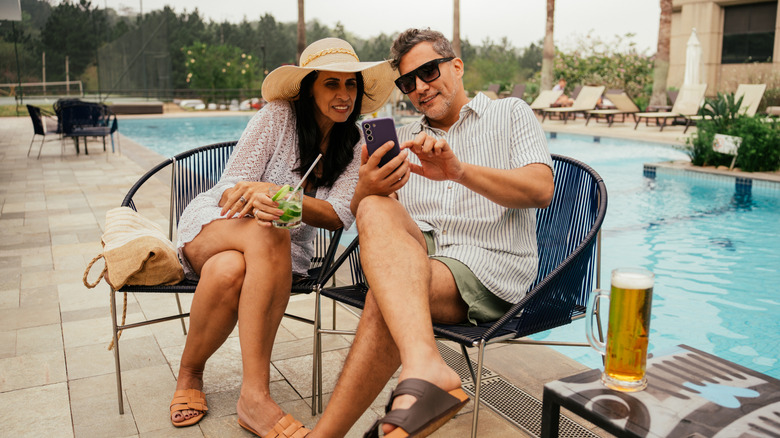 A mature couple looking at a shared phone poolside.