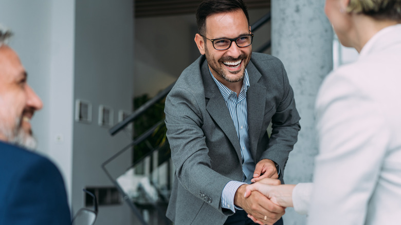 A smiling man shaking the hand of an employer after receiving a raise.