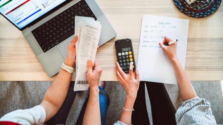 Two women calculating their bills and expenses using a calculator and laptop.