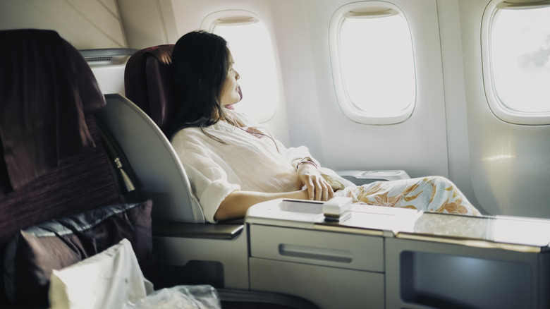 A relaxed first class passenger is looking out of the window of a passenger aircraft.