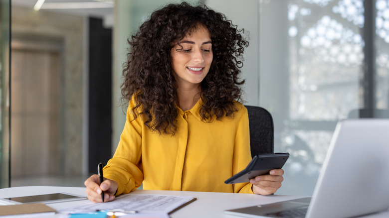 A happy Millennial women crunching numbers on a calculator.