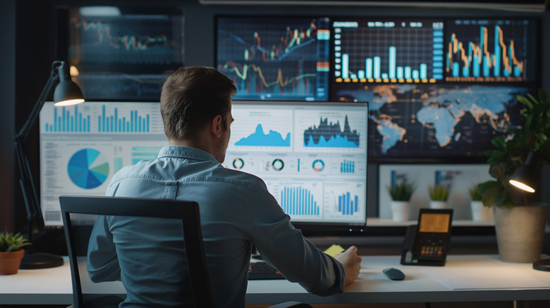 A man sitting in front of a wall of screens showing stock graphs and charts.