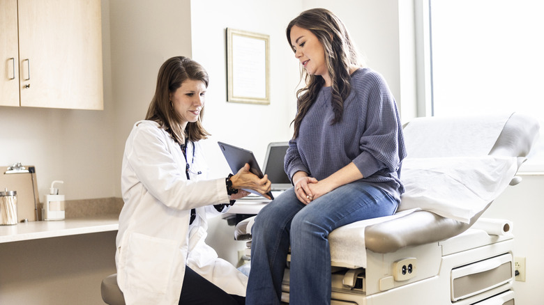Female doctor discussing treatment on digital tablet with female patient in exam room.