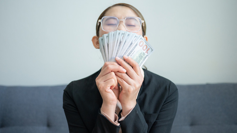 A woman sitting on a sofa with a bundle of U.S. dollars in front of her face.
