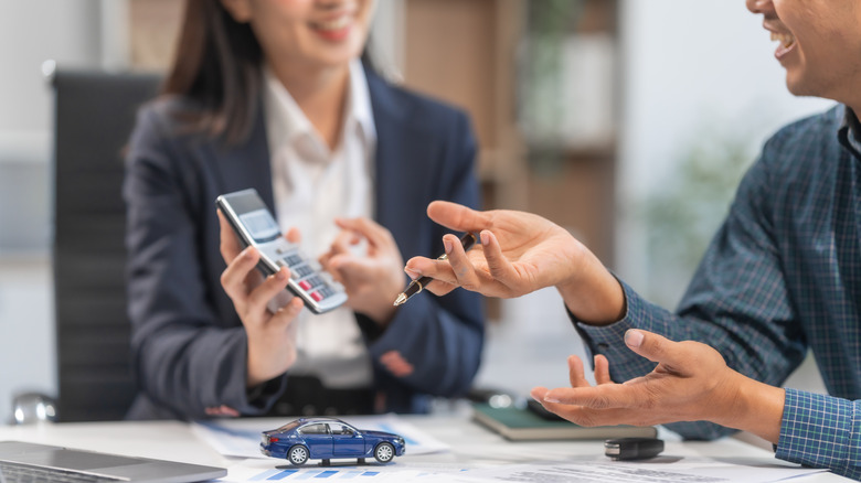 A car saleswoman showing a car price on a calculator to a potential buyer.