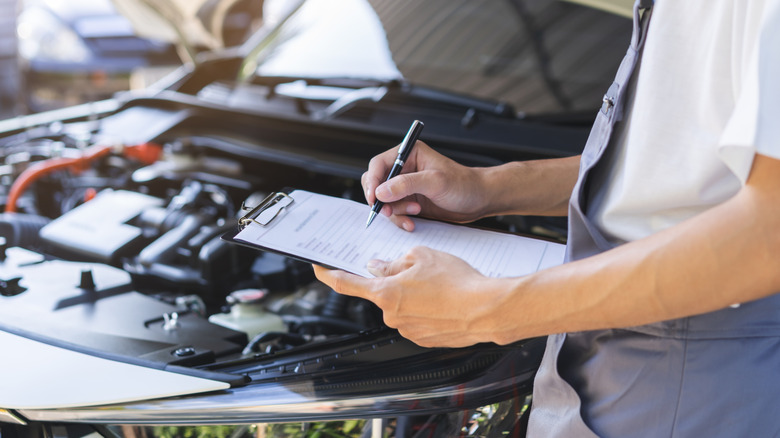 Automobile repairman writing job checklist on clipboard.