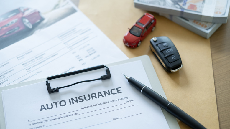 Car insurance document with pen and car key on desk.