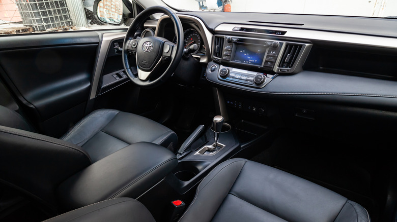 The interior of the car Toyota Rav4 with a view of the steering wheel, dashboard, seats and multimedia system with black leather trim and the letter-shaped emblem.