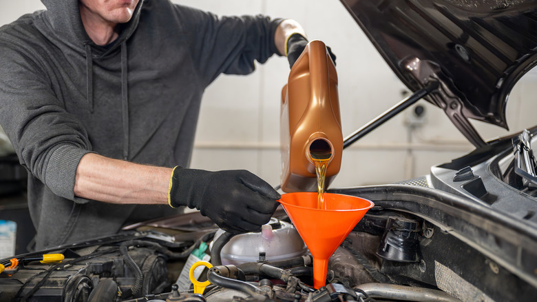 Mechanic in gloves pouring motor oil into a car engine using an orange funnel.