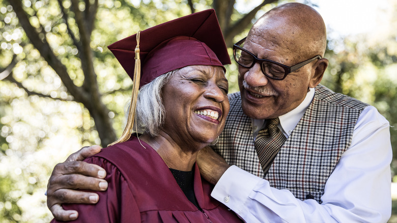 An elderly man praising an elderly woman in a graduation gown and cap.