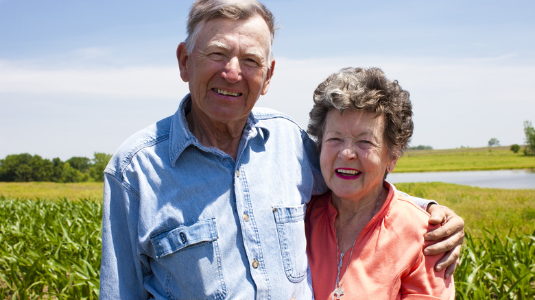 A smiling elderly couple hugging in a corn field.