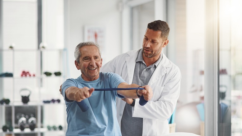 An elderly man using tension bands with the assistance of a physiotherapist.