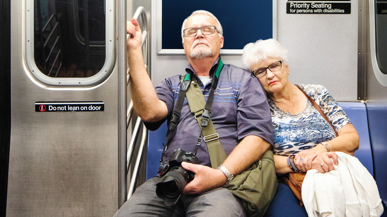 A tired senior couple asleep on a train.