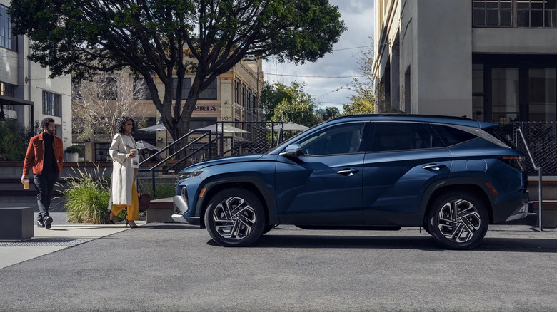 blue Hyundai Tucson parked on a city street as well-dressed couple approaches from the left