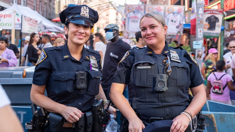 A pair of smiling women police officers standing in front of a crowd in New York City.