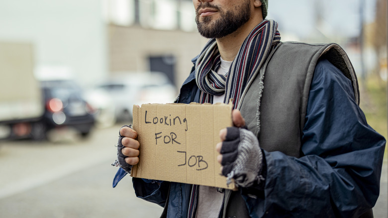 Man in fall/winter clothes holds sign that reads "looking for job"