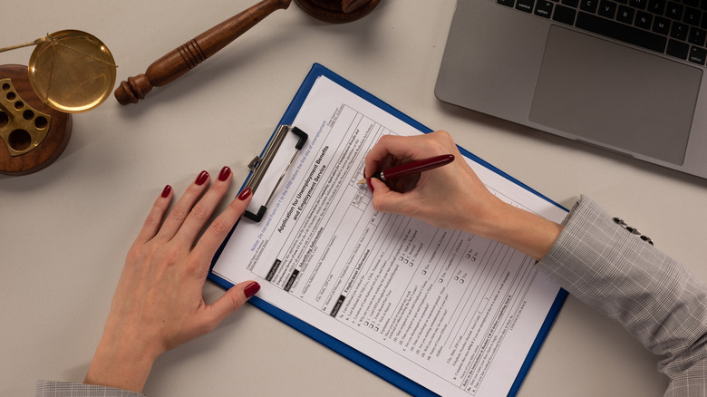 Above shot of woman filling out unemployment documents, surrounded by legal scale, judge's gavel, and laptop