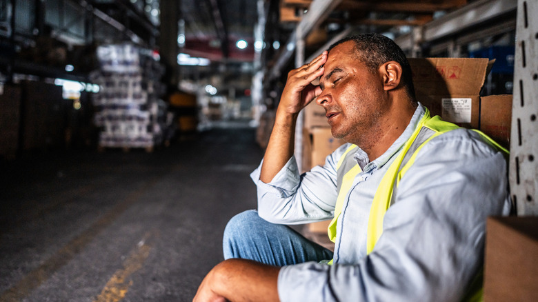 Tired man sitting in front of boxes in dark and empty warehouse
