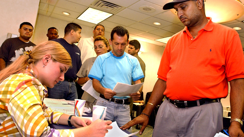 Man stands in front of woman seated at table with line of people behind him