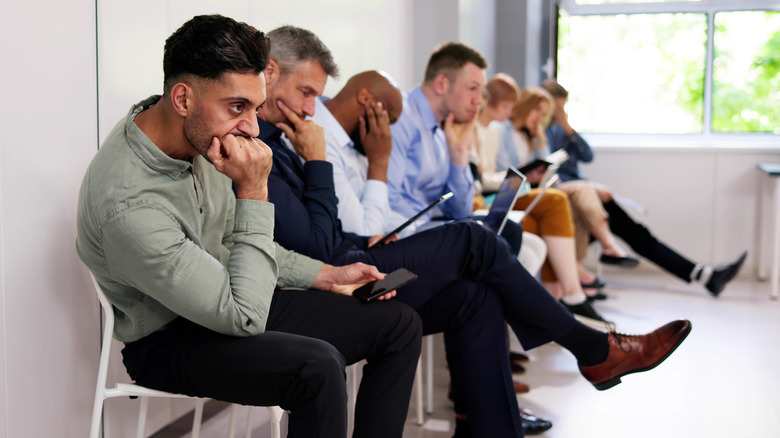 People sit in chairs anxiously waiting in a room with an open window