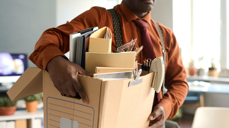 Man holds box filled with office items as he leaves room