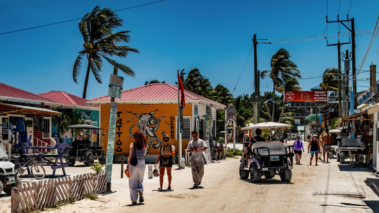 An unpaved an street with golf cart taxi and pedestrians on a sunny day