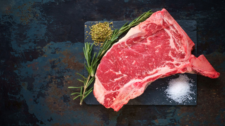 A fresh raw striploin steak on the stone with the salt, garlic and herbs on iron background.