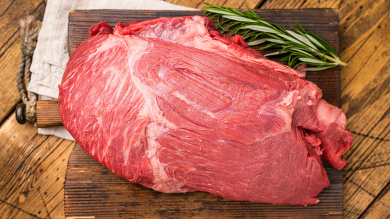 Raw Round beef meat cut, on wooden board with rosemary.