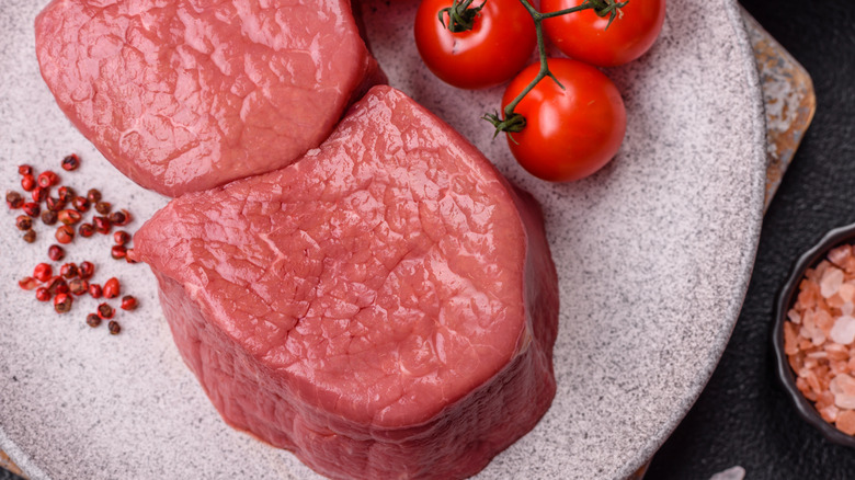 Angus beef eye round steak raw with salt, spices, tomatoes, and herbs.