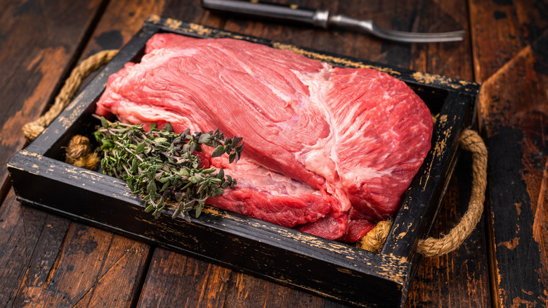 An top round roast raw with thyme in wooden tray.