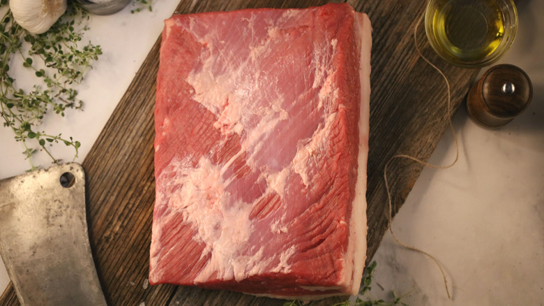 Angus whole beef brisket raw on wooden board, knife, and herbs.